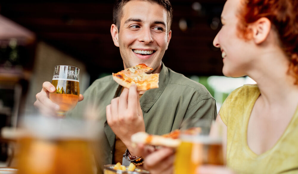 Young,Happy,Couple,Eating,Pizza,And,Drinking,Beer,While,Talking
